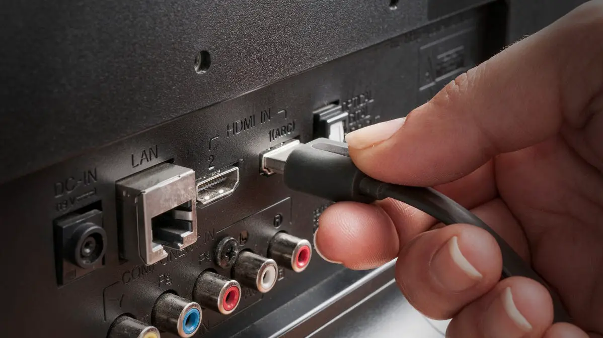Someone plugging an HDMI connector into a TV set.